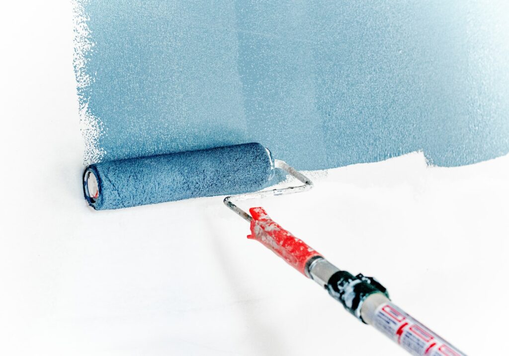 un rullo dipinge una parete con pittura antimuffa di blu dopo averla ripulita dalla muffa