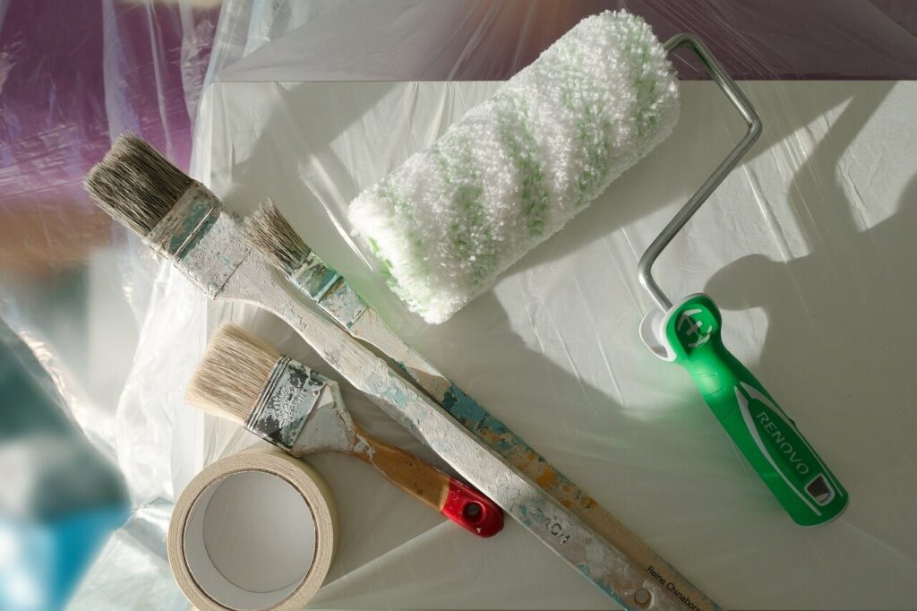 strumenti per ristrutturazione appartamento: un rullo per pittura, un pennello, nastro adesivo