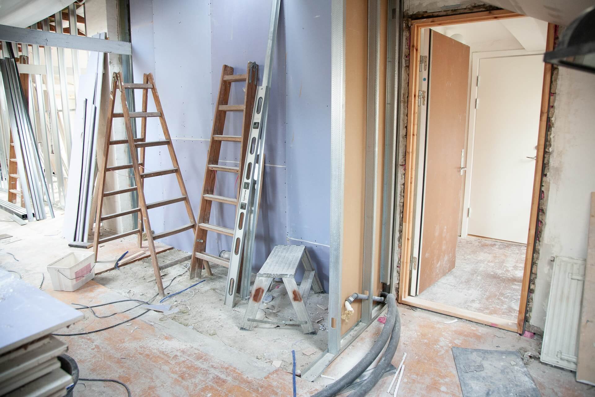 una stanza in rifacimento con scala di legno appoggiata al muro e strumenti utilizzati per la ristrutturazione casa sul pavimento