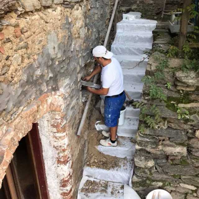 un muratore esegue lavori di ristrutturazioni casa lavorando su un muro esterno fatto in pietra